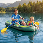 A man and a child enjoy a sunny day on a lake, sitting in a green inflatable raft with yellow paddles. The man wears a blue t-shirt and the child wears a bright pink and green life vest.