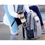 Person holding a blender next to a gray backpack on a floor.