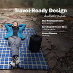 Person lying on a blue checkered travel mat with a backpack, surrounded by rocks.