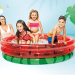Children playing in a watermelon-themed inflatable pool with a woman supervising.
