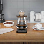 Coffee brewing setup on a kitchen counter with a bowl of coffee beans and a cup of coffee.