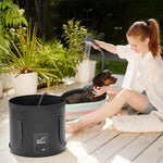 Woman washing a dog in an outdoor setting with a black bucket and shower head.