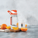 Orange-themed kitchen items including a blender and juicer on a gray surface with oranges.