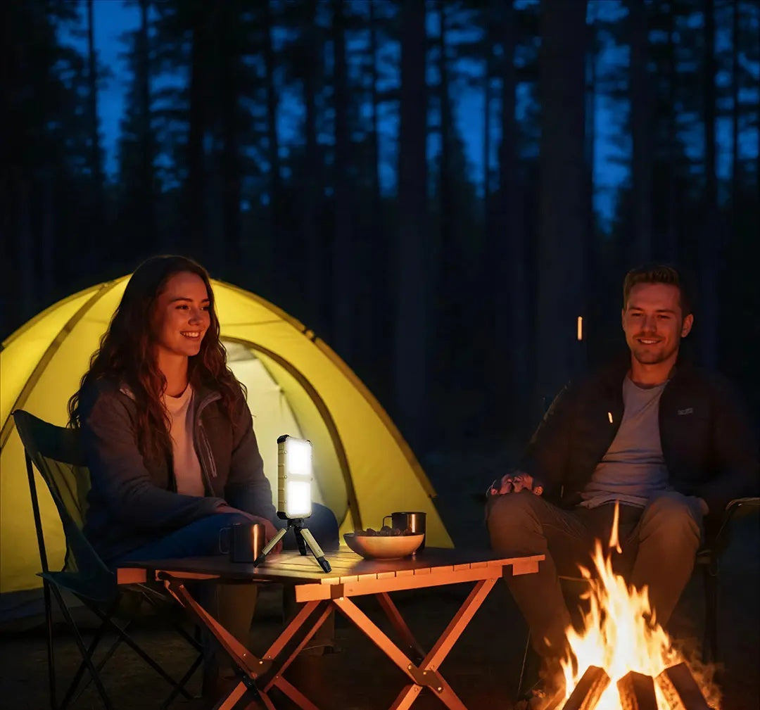 Two people sitting by a campfire at night in a forest, with a tent in the background.