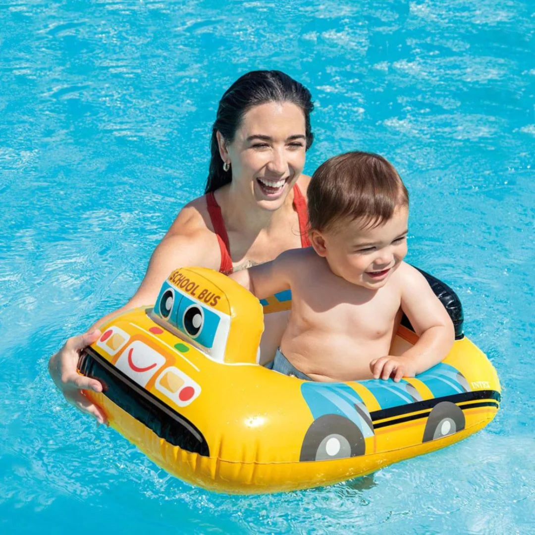 Woman and child on a yellow toy bus float in a pool