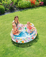 Woman and two children playing in a inflatable pool on a grassy lawn