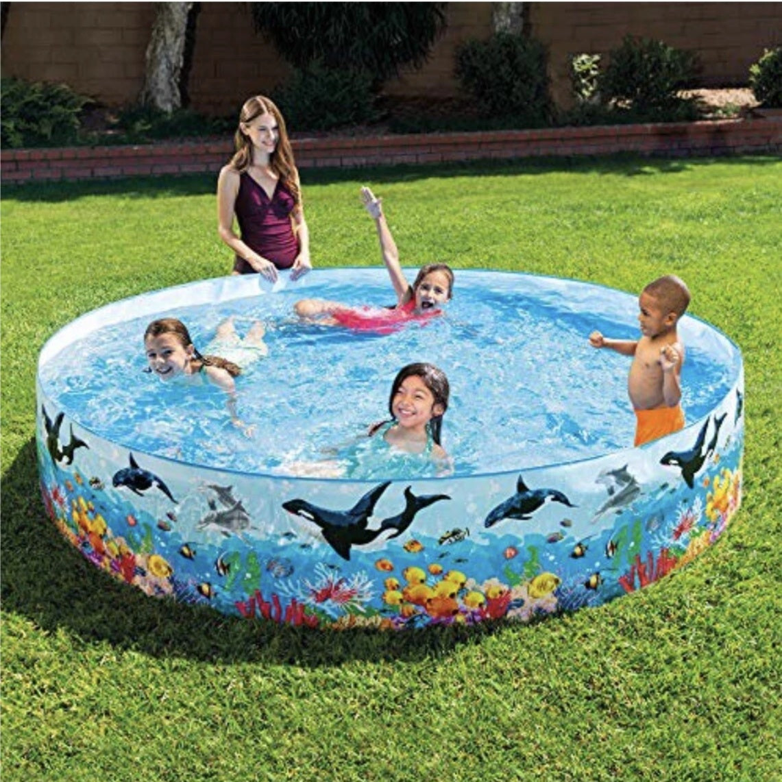 Children playing in a inflatable pool with ocean design on a grassy area.