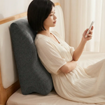 Woman using a backrest pillow on a bed while holding a phone.