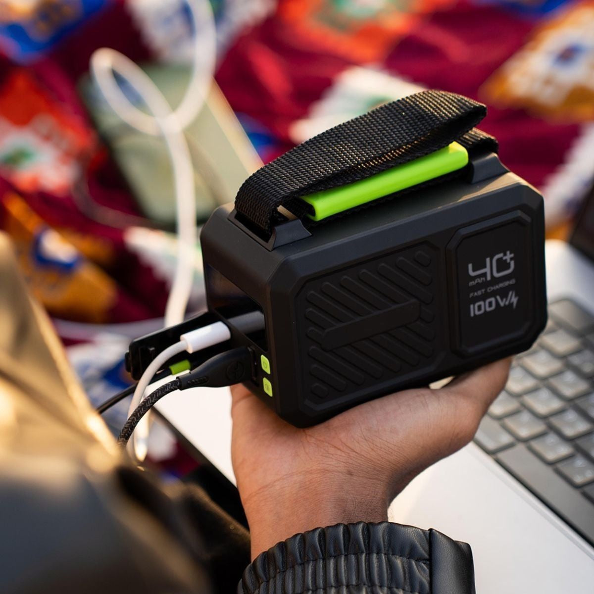 Hand holding a black power bank with green accents, connected to a device, on a colorful background.